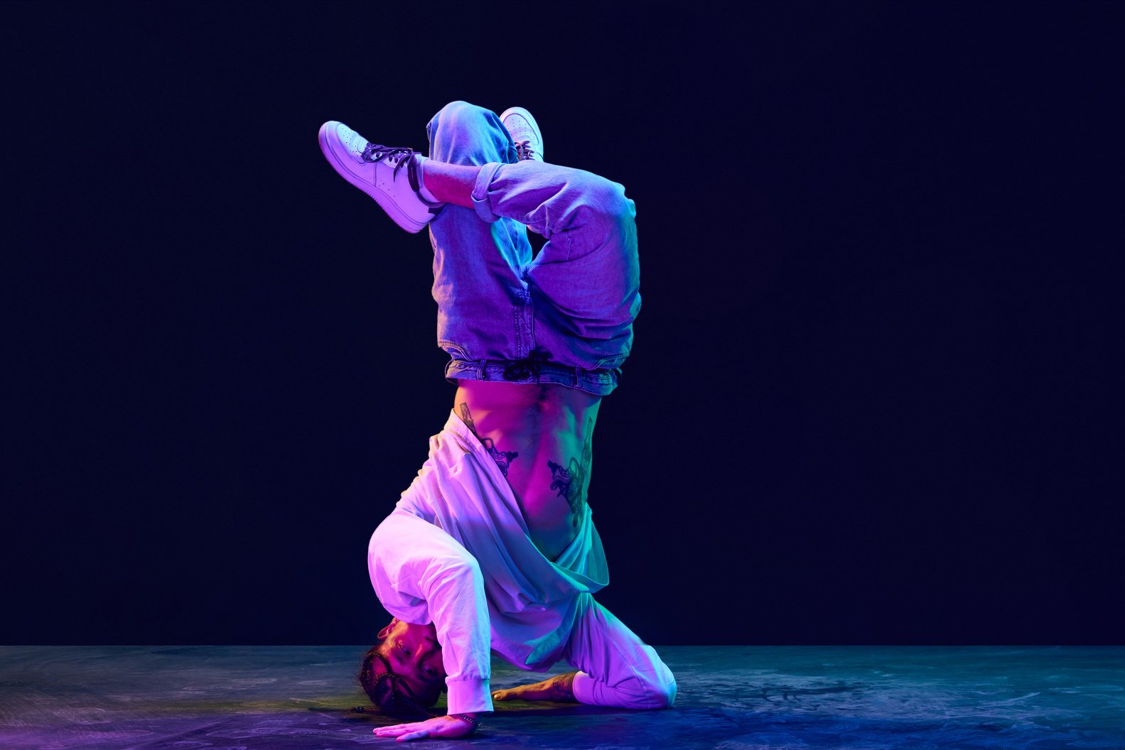 Artistic, sportive young man in sprotive clothes dancing breakdance, hip-hop against black studio background in neon light